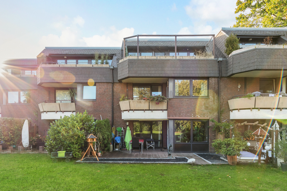Rückseite eines Mehrfamilienhauses mit Balkonen, Terrasse und grüner Wiese im Vordergrund.