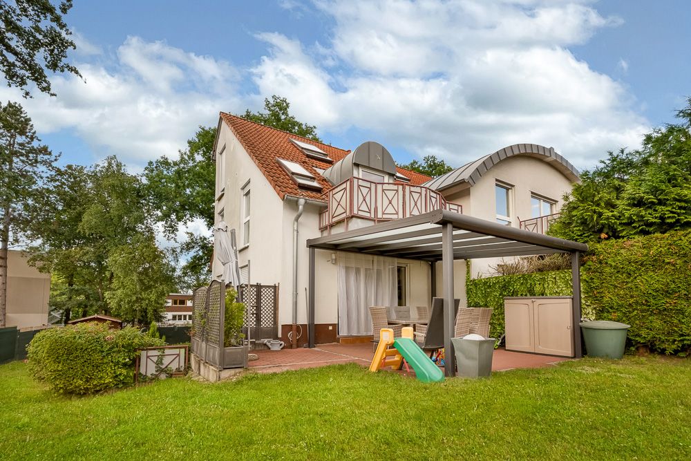 Zweistöckiges Wohnhaus mit rotem Dach, Terrasse, Gartenmöbeln und Kinderrutsche im Garten.
