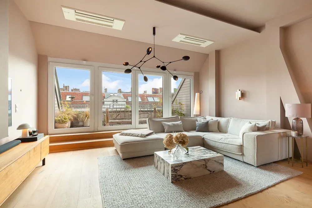 Helles Wohnzimmer mit großem Sofa, Marmortisch und großen Fenstern mit Blick auf Dächer.