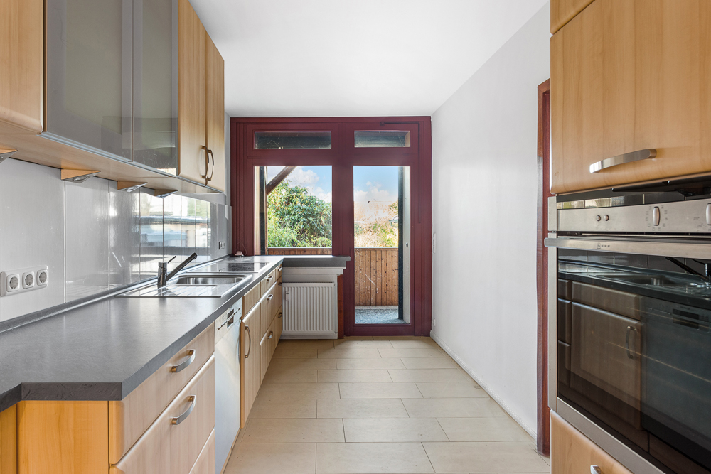 Moderne Küche mit Holzmöbeln, zwei Öfen und großem Fenster zur Terrasse.