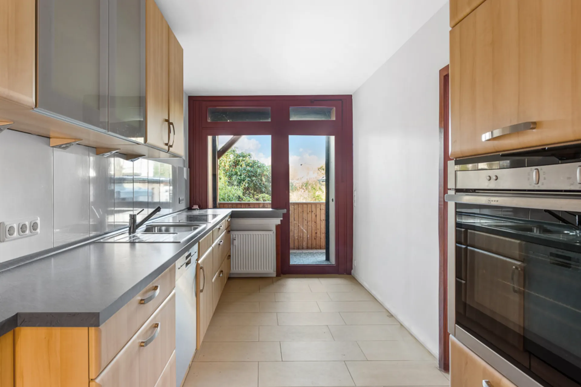Moderne Küche mit Holzmöbeln, zwei Öfen und großem Fenster zur Terrasse.