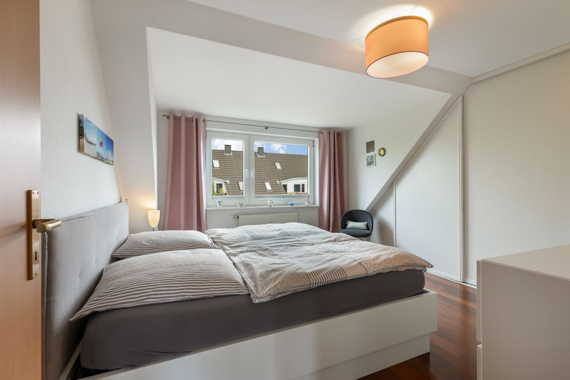 Modernes Schlafzimmer mit Doppelbett, Fenstern und rosa Vorhängen.
