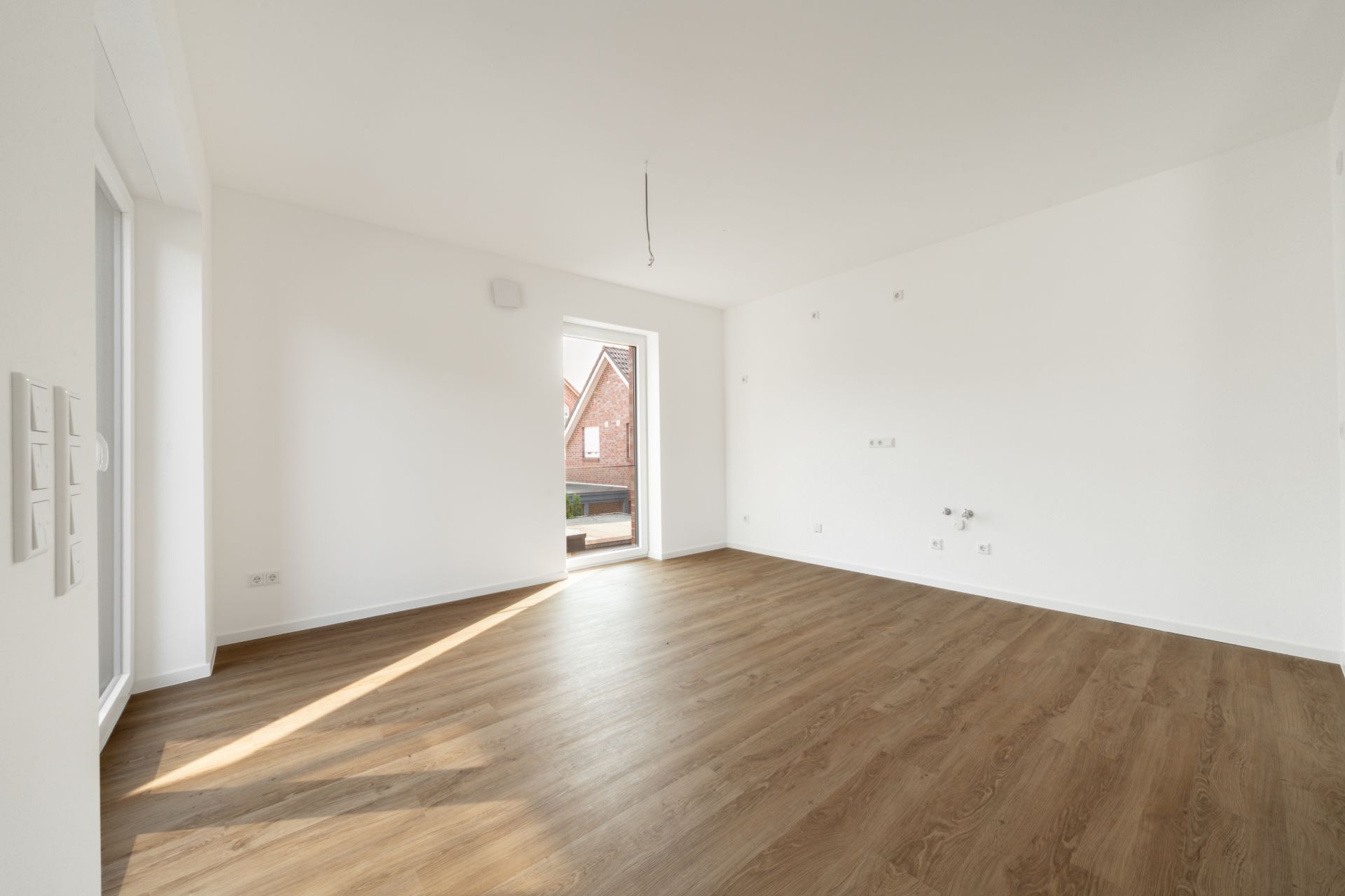 Heller, leerer Raum mit Holzfußboden und weiß gestrichenen Wänden, Tür zum Außenbereich.