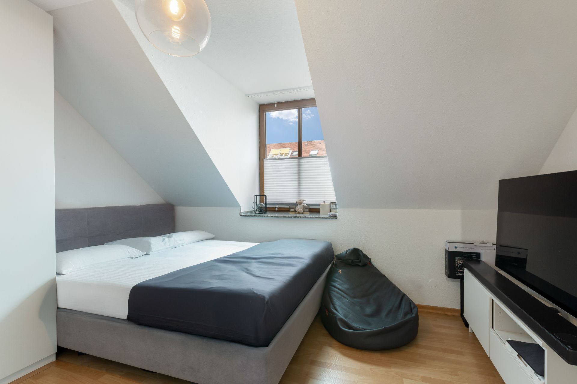 Schlafzimmer mit Doppelbett, Fernseher, Sitzsack und Fenster unter Dachschräge.
