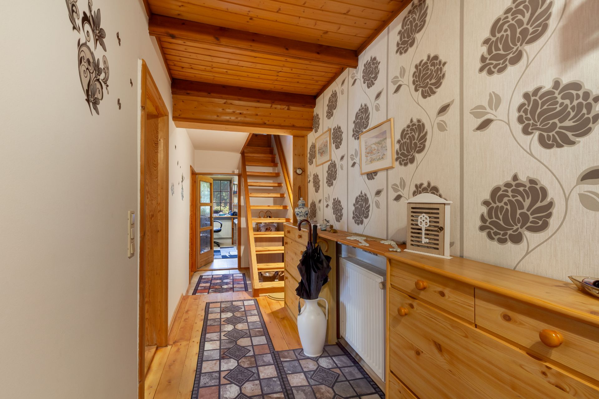 Flur mit Holzdecke, gemusterter Tapete, Teppichläufer und offener Treppe nach oben.