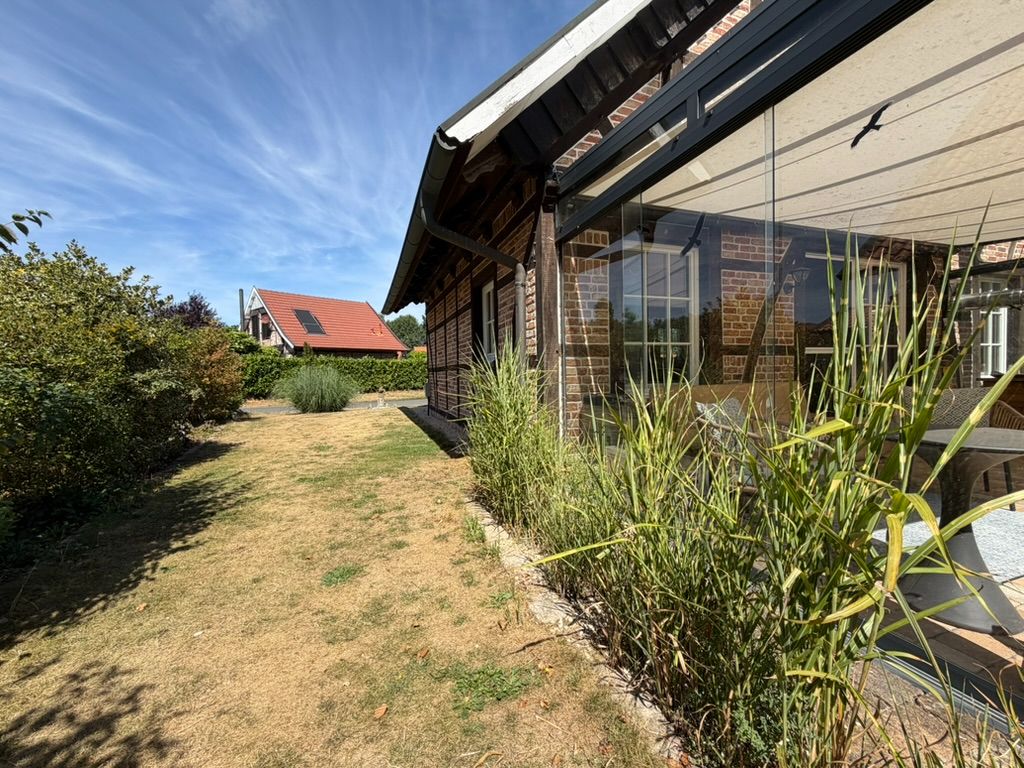 Garten mit Rasenfläche und Glasveranda an einem Backsteinhaus, Pflanzen am Rand.
