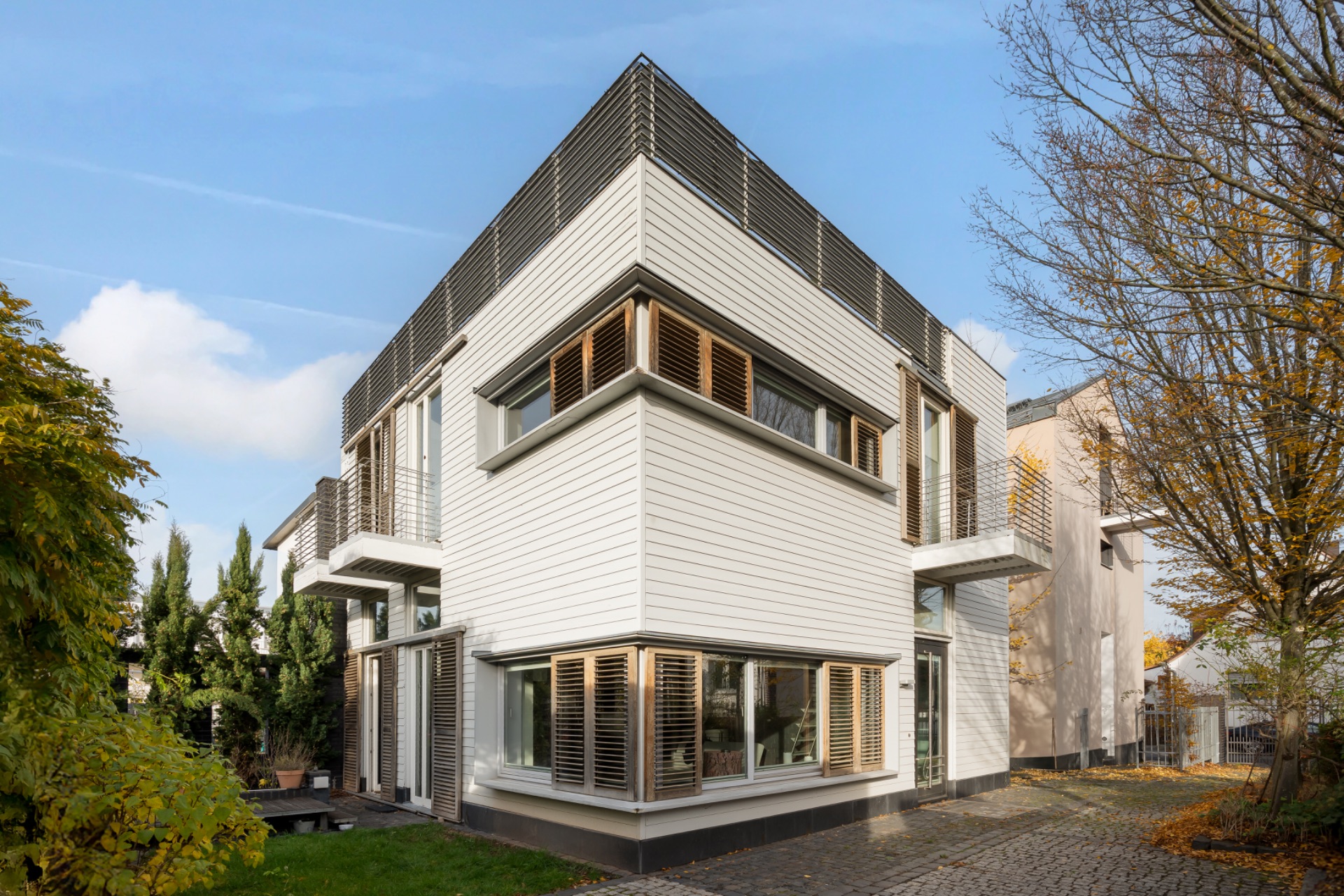 Modernes zweistöckiges Wohnhaus mit großen Fenstern und Holzlamellen, umgeben von Bäumen.