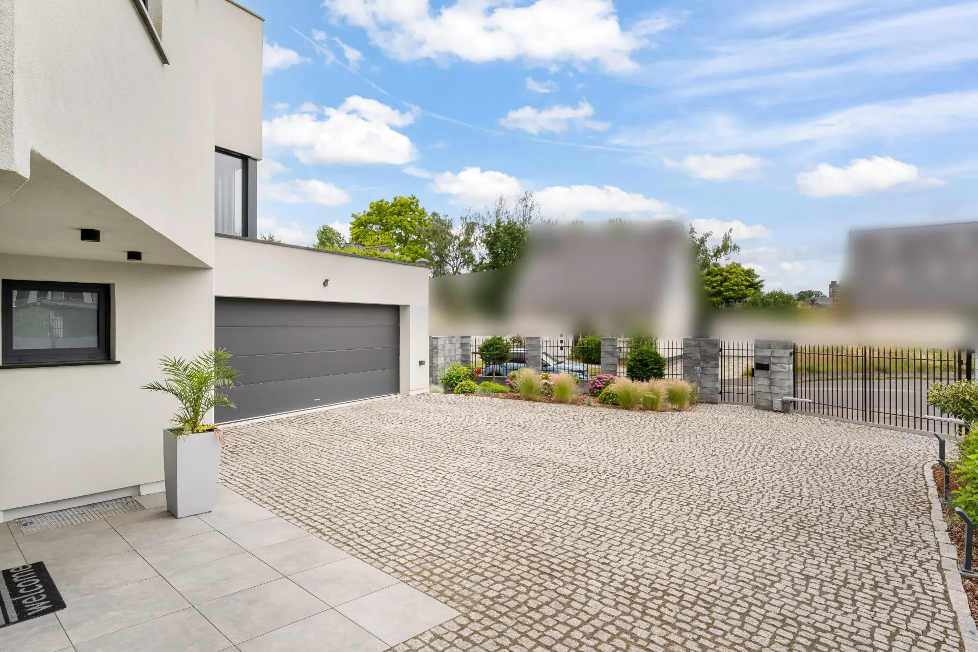 Moderner Hausvorplatz mit gepflasterter Einfahrt, Garage und einigen Pflanzen.