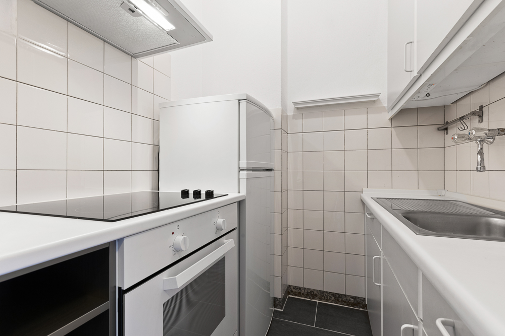 Kleine weiße Küche mit Herd, Ofen, Kühlschrank und Spüle.