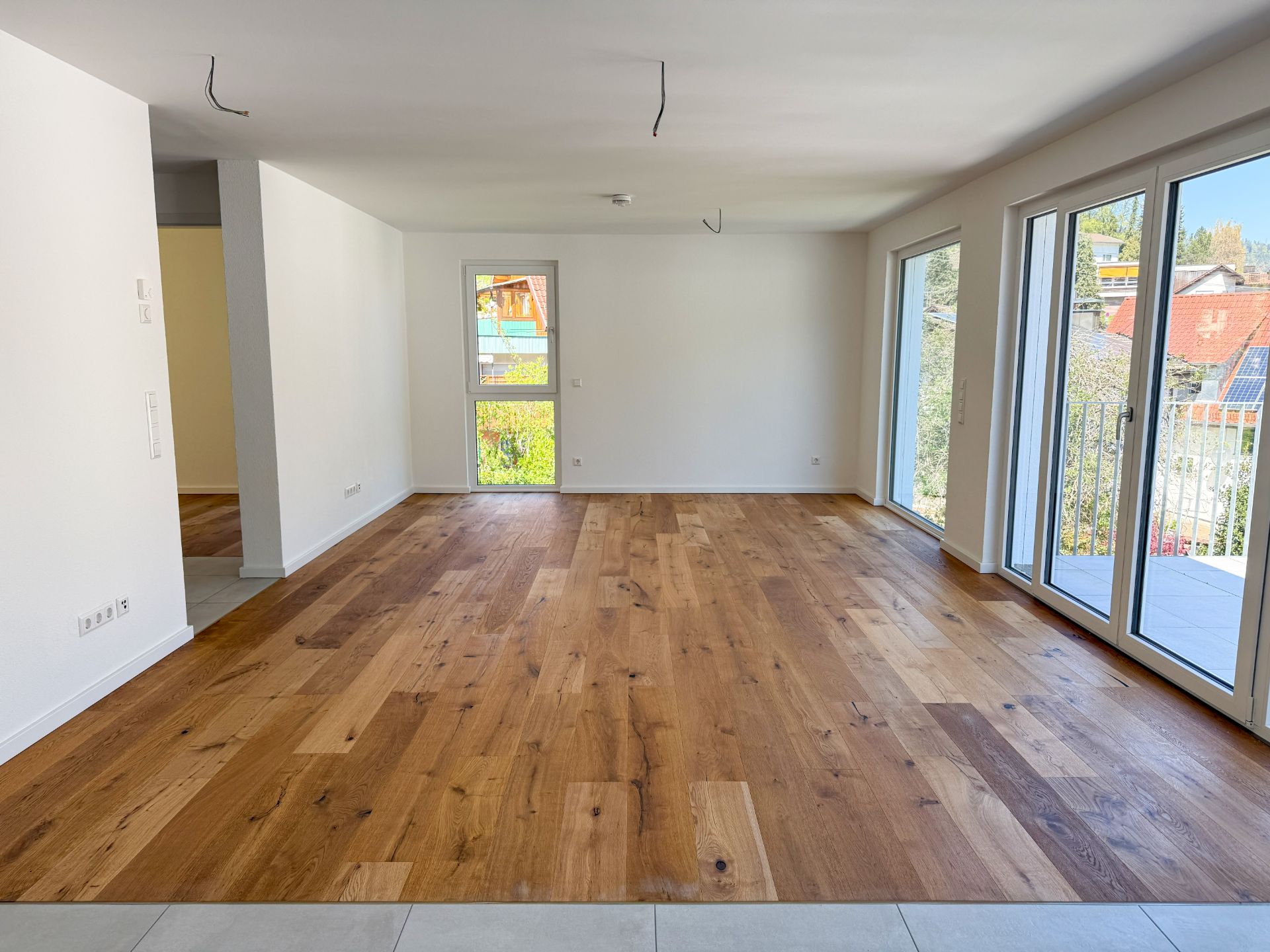 Helles Wohnzimmer mit Parkettboden und großen Fenstern, Zugang zum Balkon.