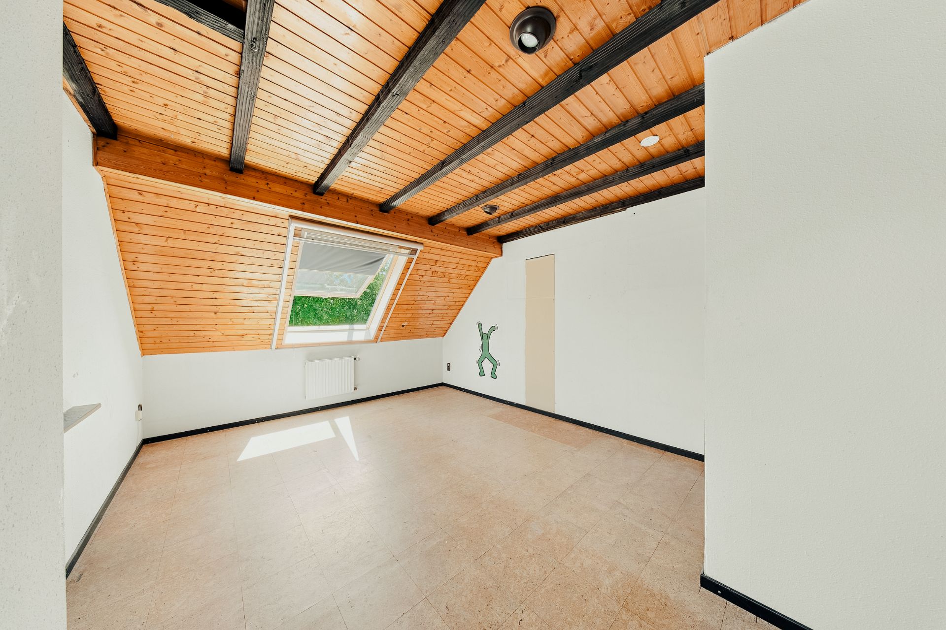 Leerer Raum mit Holzdecke, schwarzem Gebälk und großem Dachfenster.