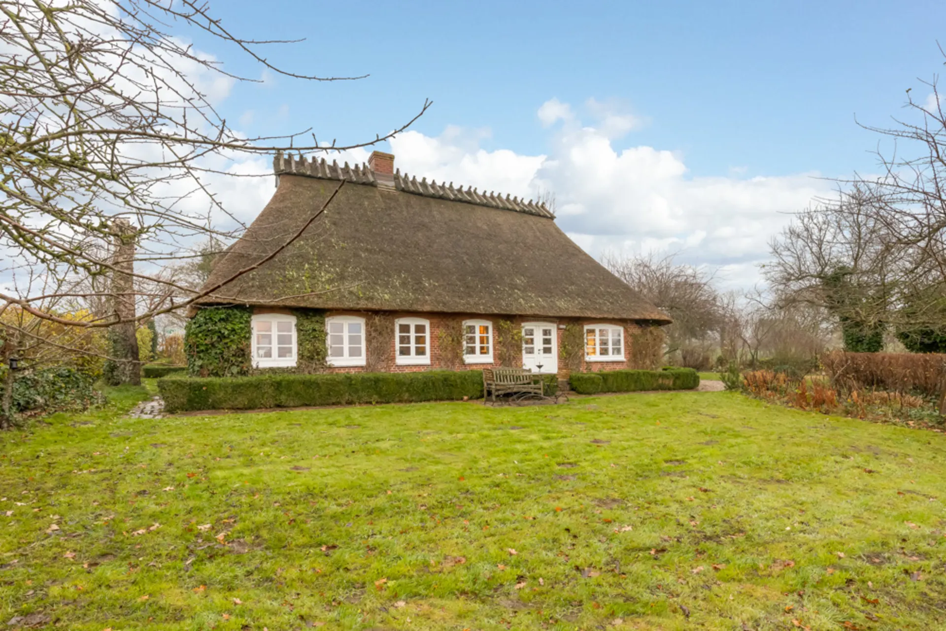 Typisches reetgedecktes Haus mit Gartenbank und viel Grünfläche im Vordergrund.