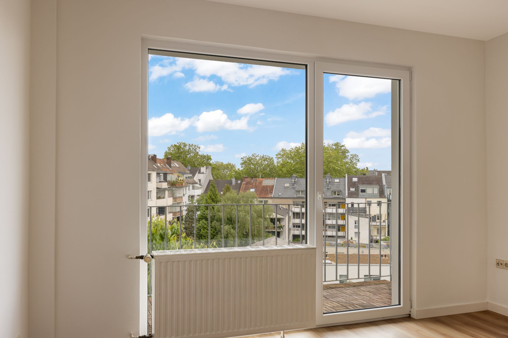 Helle Wohnzimmerecke mit großem Fenster und Blick auf einen Balkon und Wohngebäude.