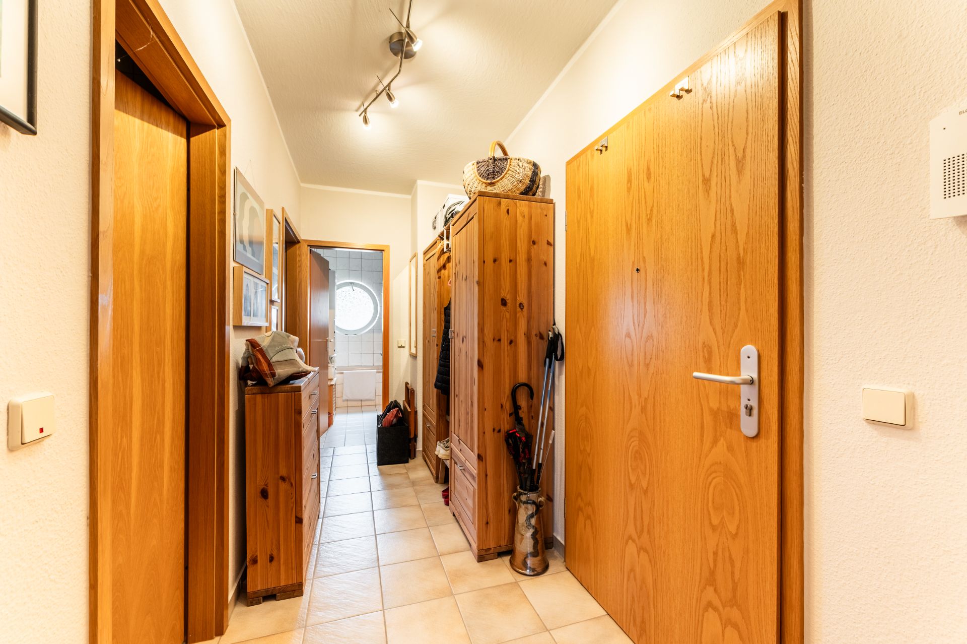 Heller Flur mit Holztüren, Holzschränken, Fliesenboden und Garderobe.
