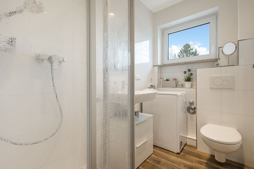 Modernes Badezimmer mit Dusche, Waschbecken, Waschmaschine, Fenster und Wand-WC.