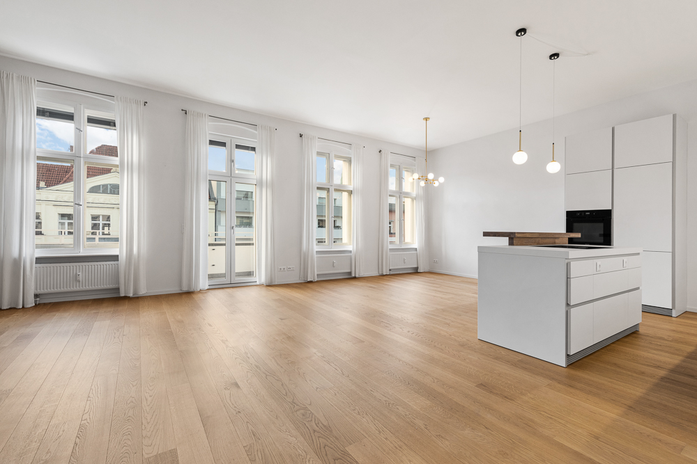 Helles, modernes Wohnzimmer mit offener Küche, großen Fenstern und Holzboden.