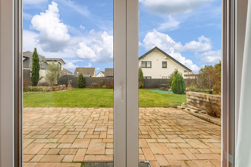 Blick durch eine Glastür auf eine Terrasse und einen großen Garten mit Rasen.