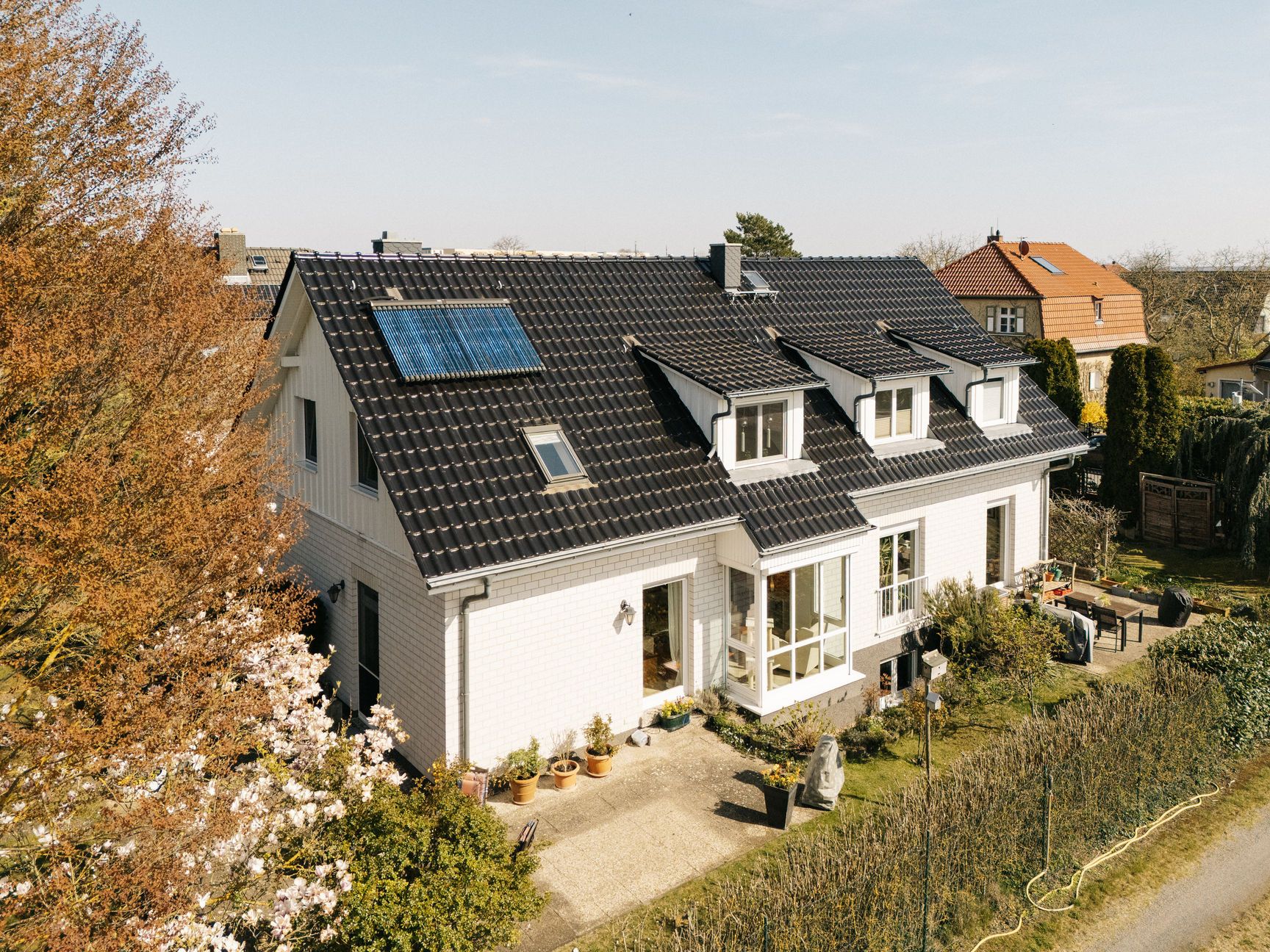Modernes Haus mit schwarzem Dach, Solarpanel und Garten, umgeben von Bäumen und Pflanzen.