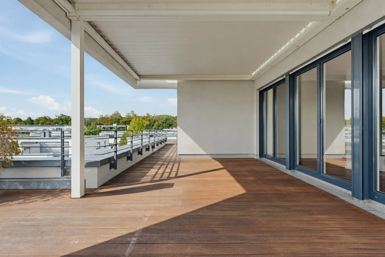 Große Terrasse mit Holzfußboden, Glasgeländer und bodentiefen Fenstern.