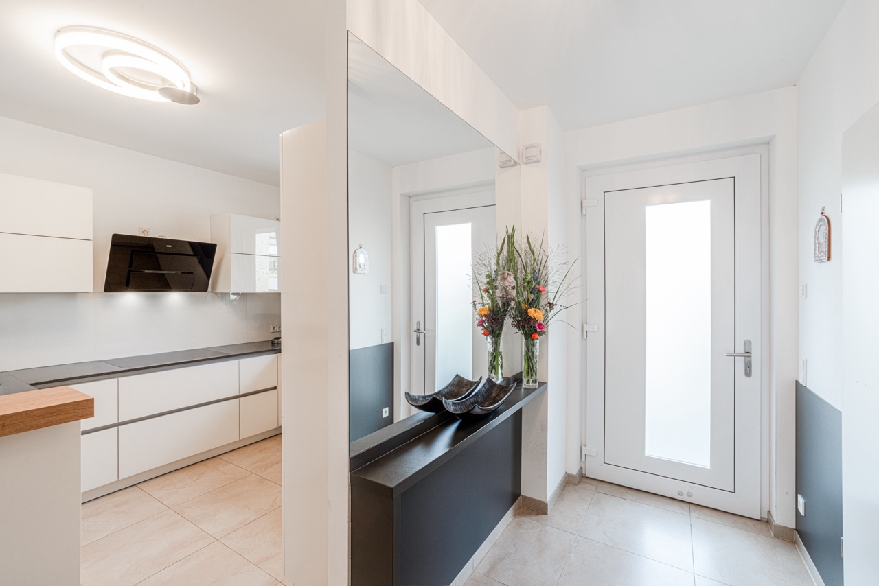 Heller Flur mit großem Spiegel, Konsole, Blumenvasen und Blick in die moderne Küche.