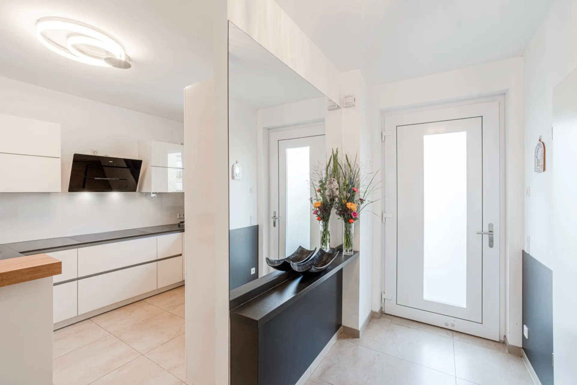 Heller Flur mit großem Spiegel, Konsole, Blumenvasen und Blick in die moderne Küche.