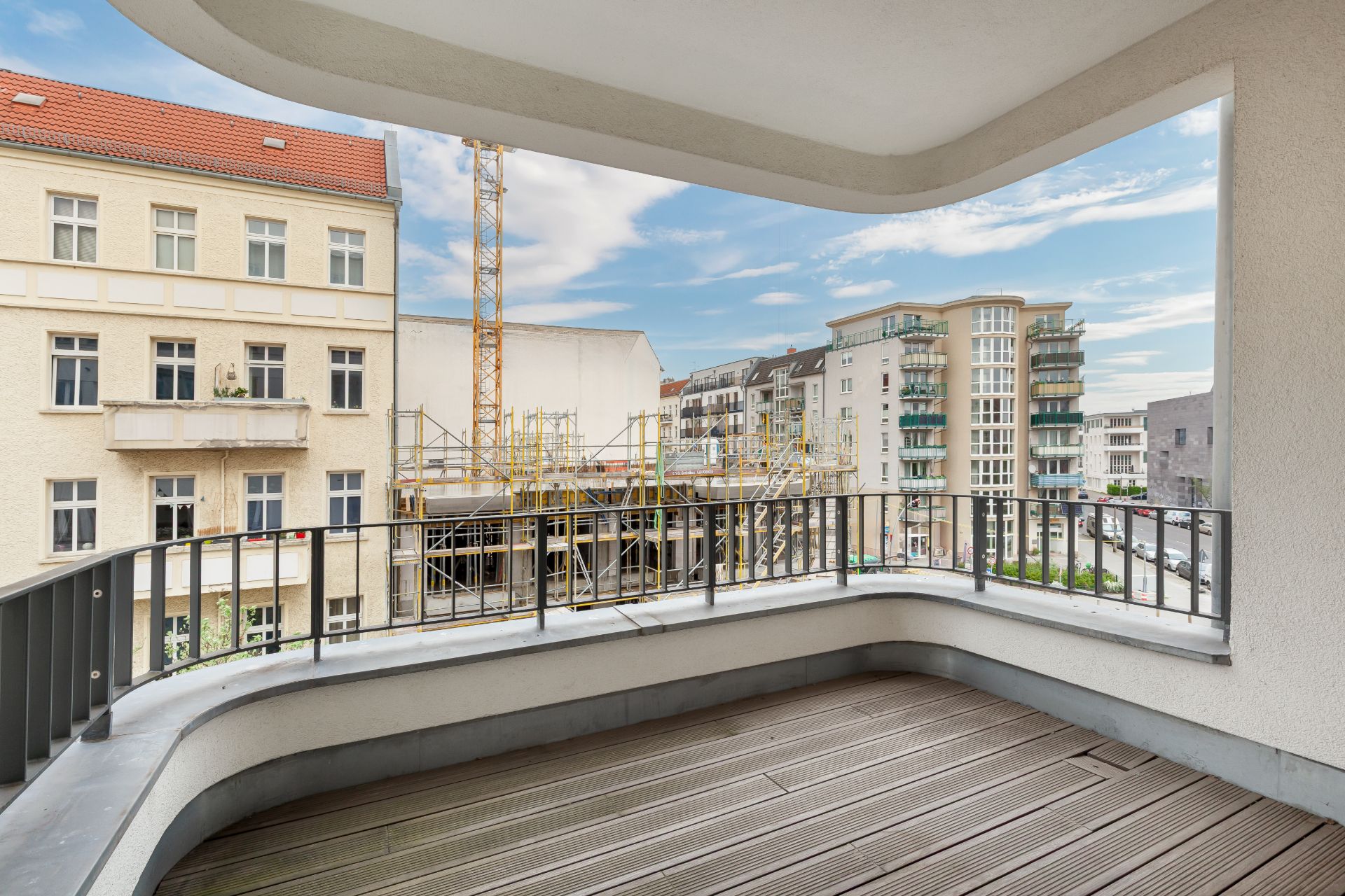 Großer Balkon mit Blick auf Straßenszene, Baugerüst und benachbarte Wohngebäude.