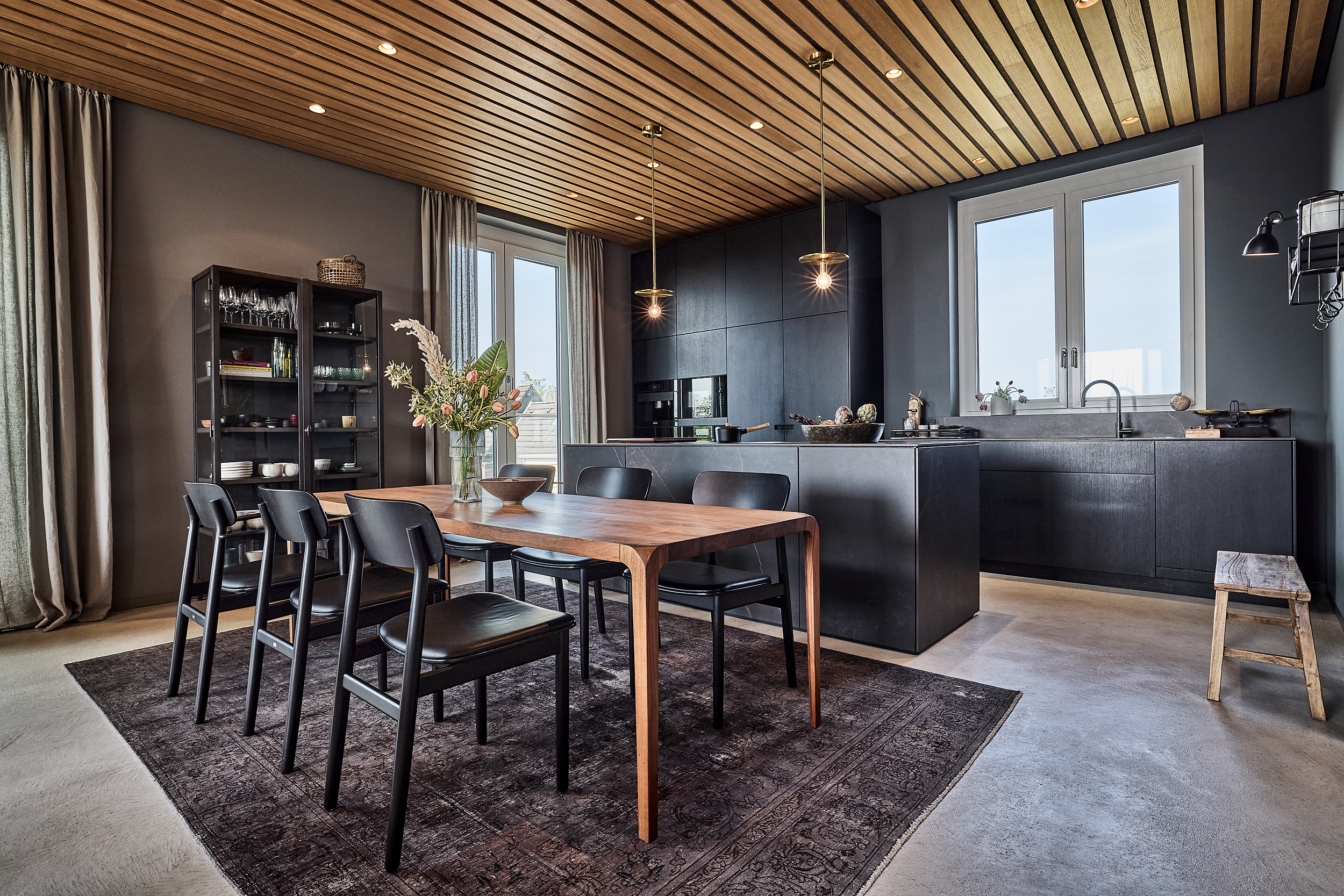 Moderne Küche mit Essbereich, Holztisch, sechs Stühlen und dunklen Küchenschränken.