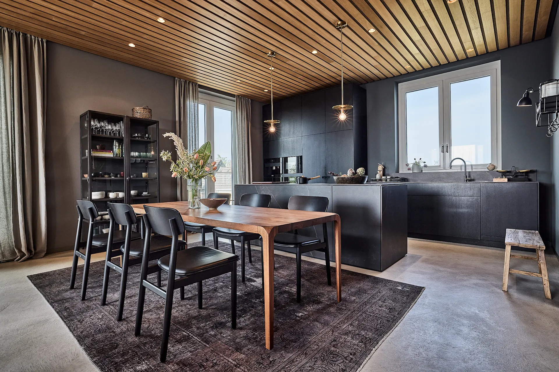 Moderne Küche mit Essbereich, Holztisch, sechs Stühlen und dunklen Küchenschränken.