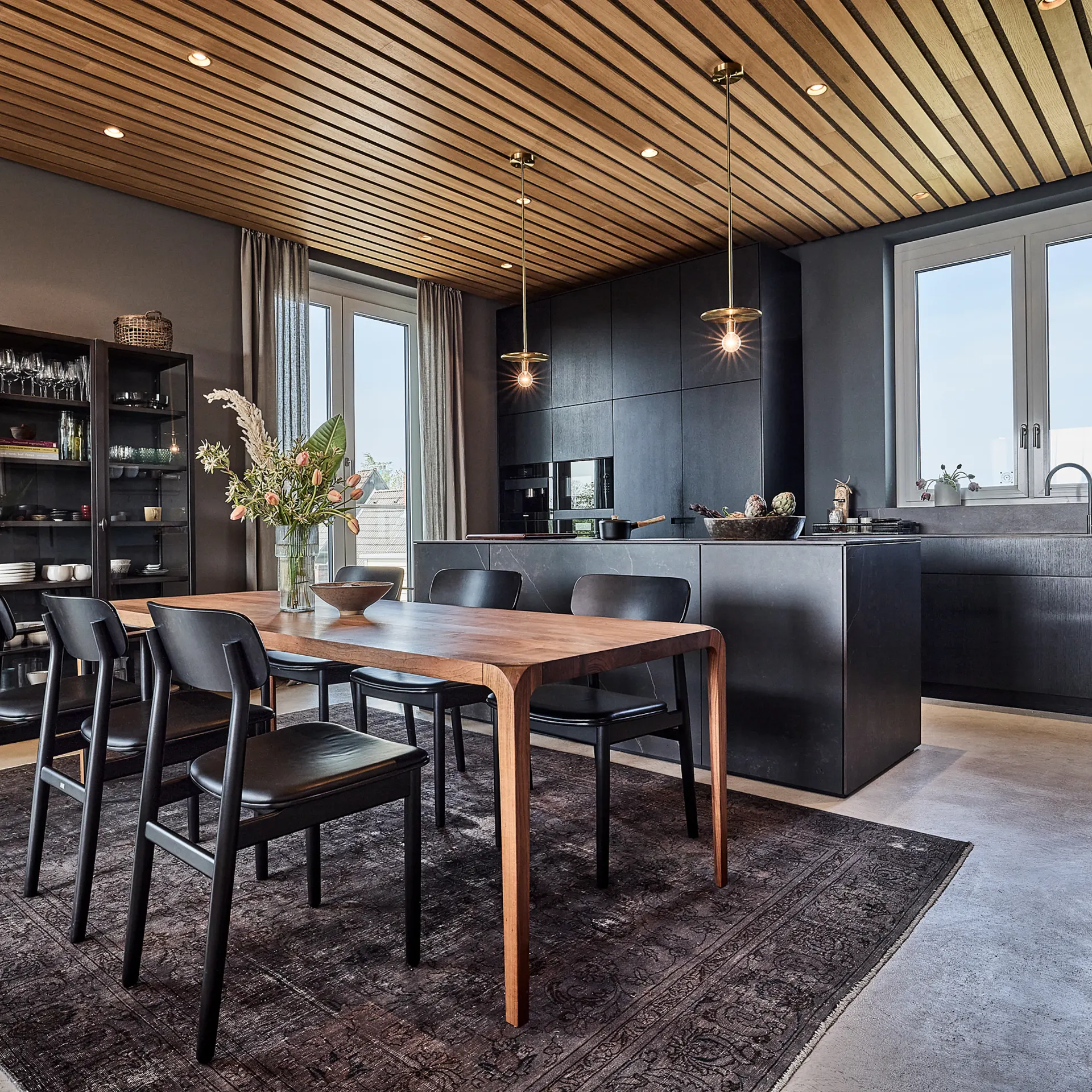 Moderne Küche mit Essbereich, Holztisch, sechs Stühlen und dunklen Küchenschränken.