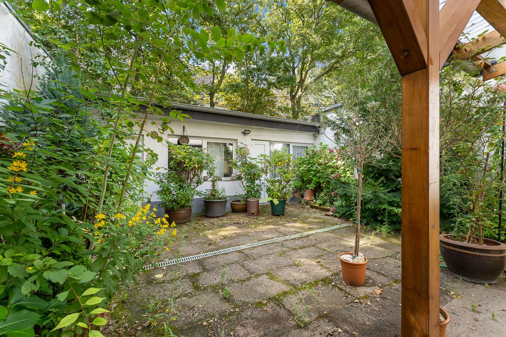 Gepflasterter Innenhof mit vielen Topfpflanzen und angrenzendem Gebäude, teils überdacht.