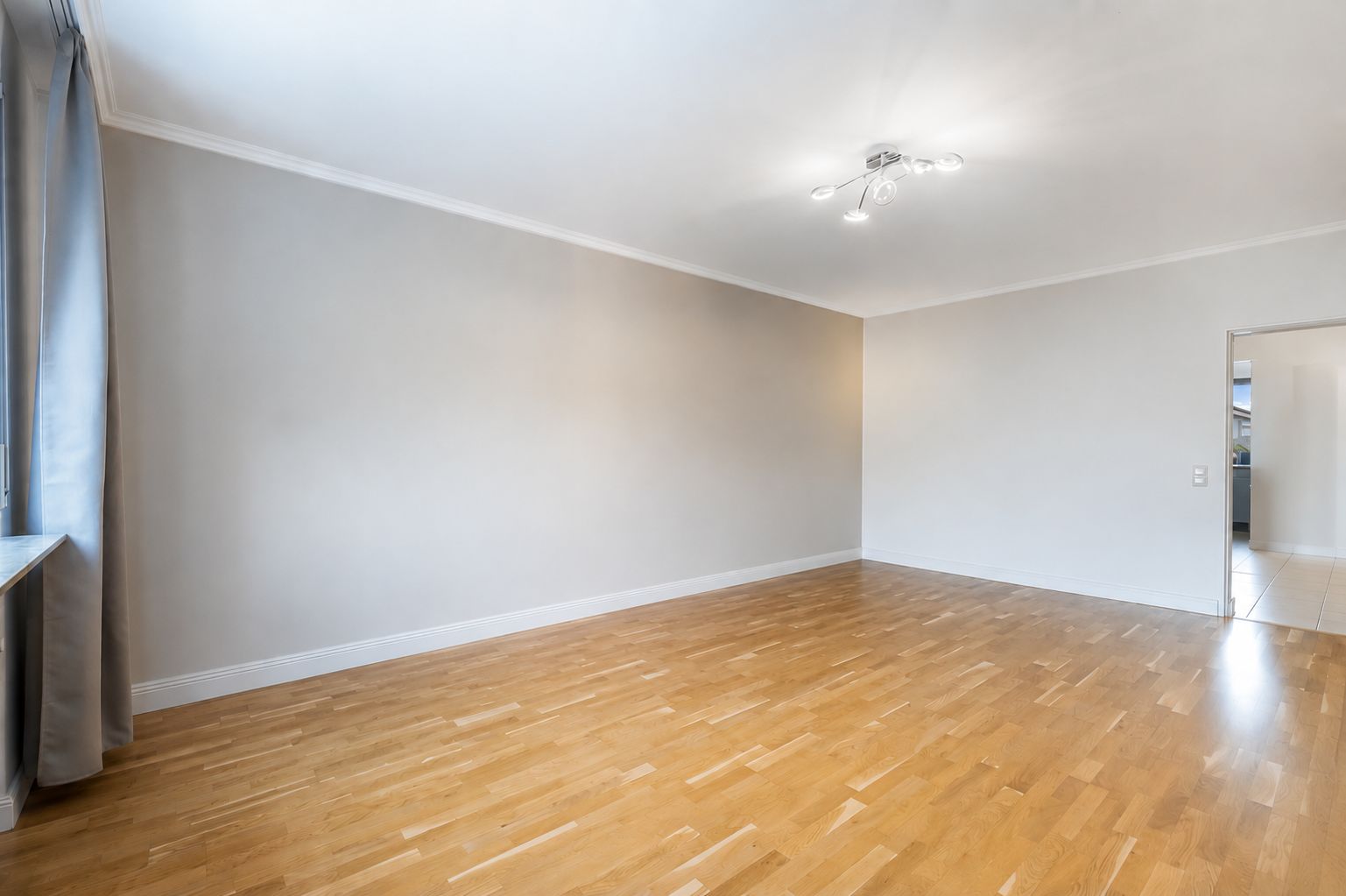 Leeres Zimmer mit Holzfußboden, weiß gestrichenen Wänden und Deckenlampe.