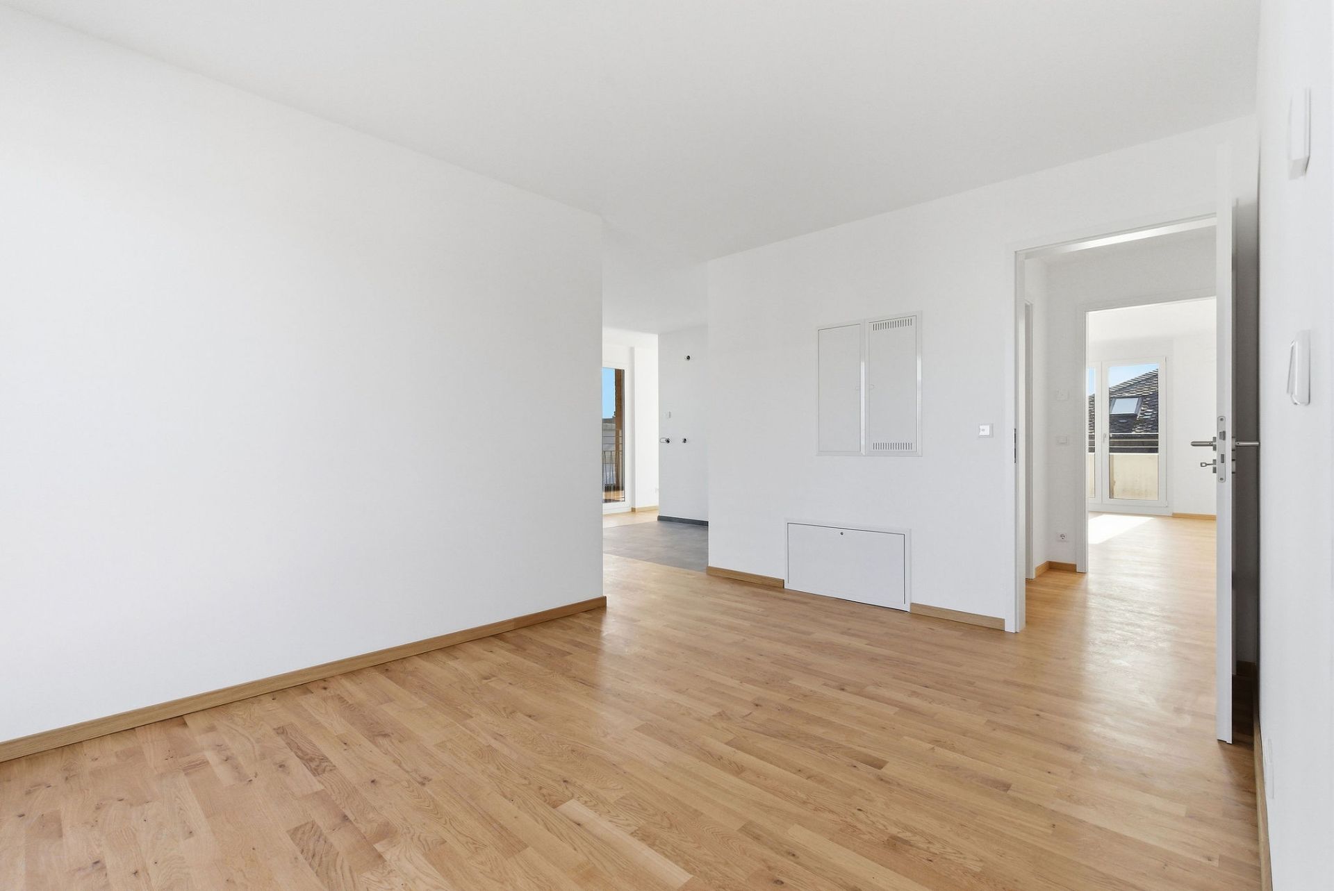 Heller Raum mit Holzboden, weißen Wänden und Türen zu weiteren Zimmern.