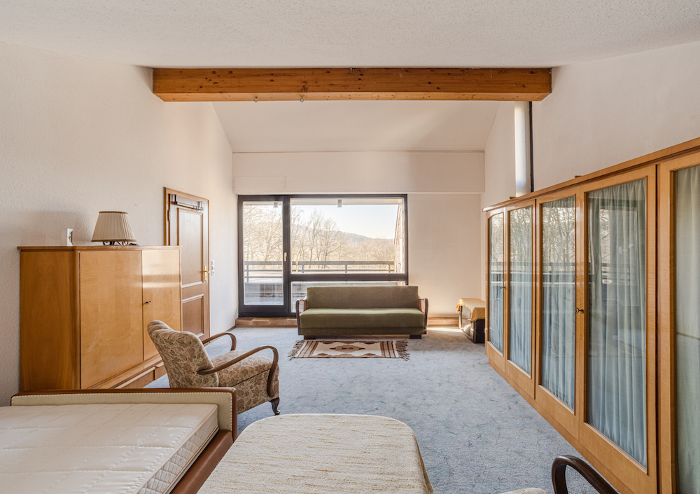 Helles Wohnzimmer mit Sofa, Sessel, Holzmöbeln und großem Fenster mit Ausblick.