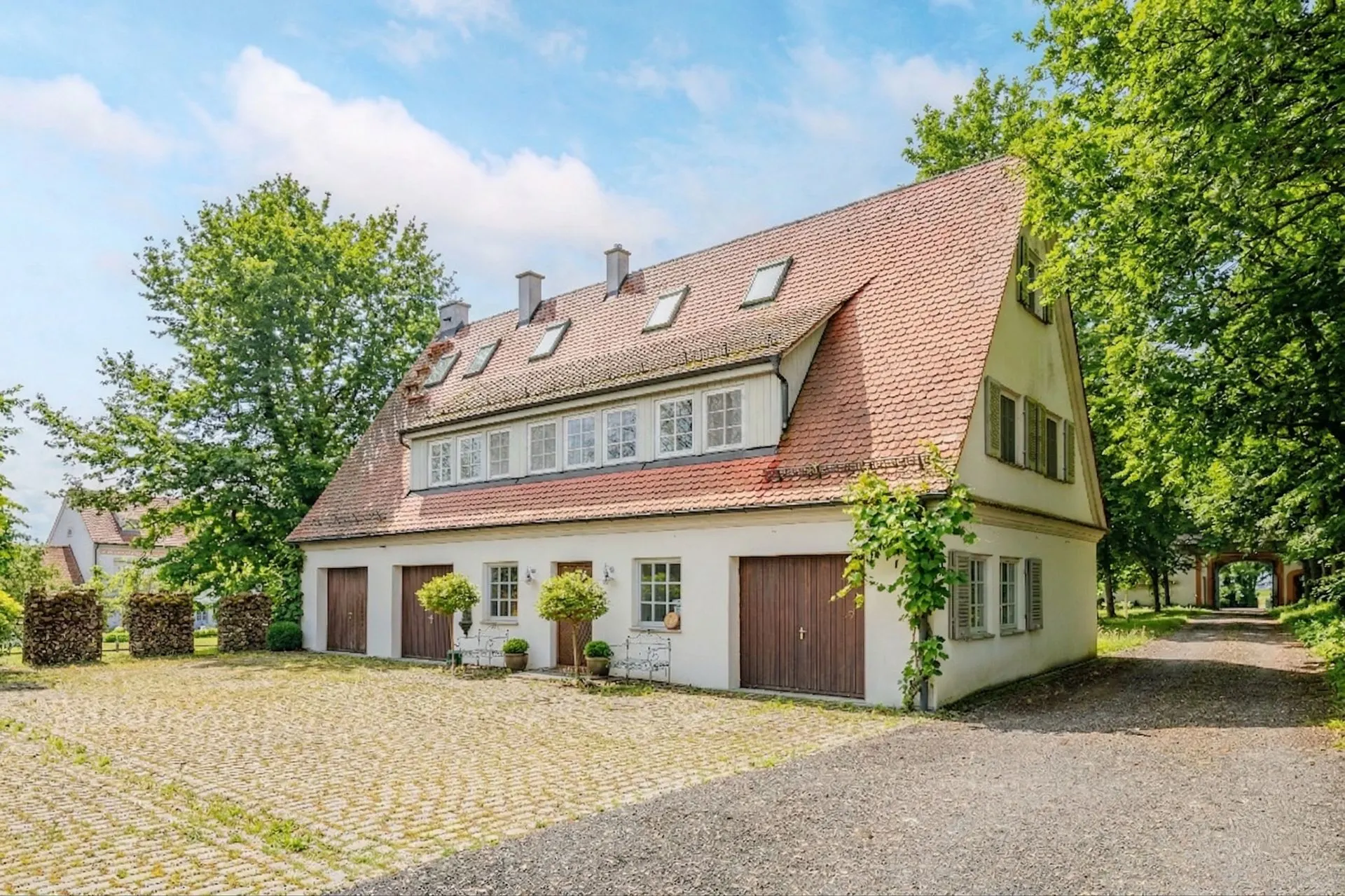 Großes Wohnhaus mit rotem Satteldach, mehreren Garagen und begrüntem Hof.