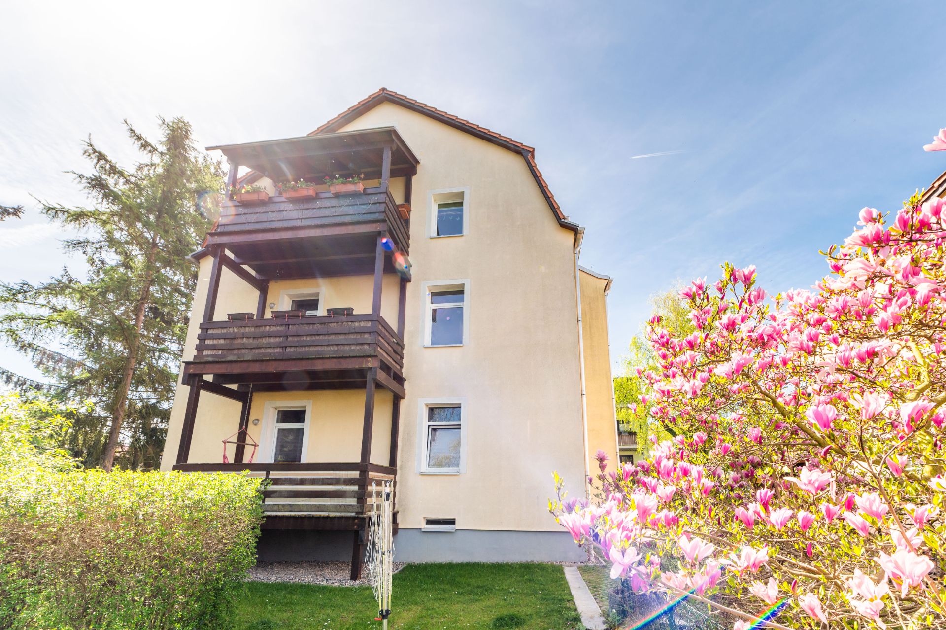 Gelbes Wohnhaus mit drei Balkonen und blühendem Baum im Garten.