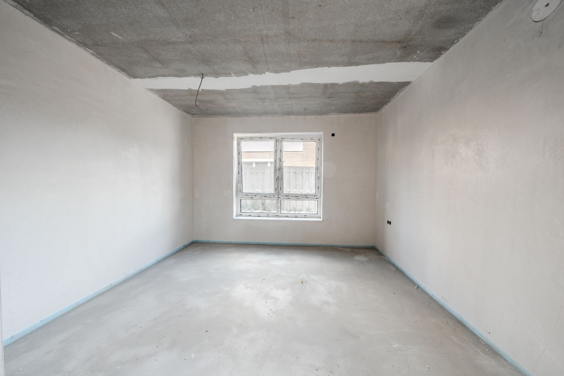 Leerer Raum mit Betonboden, weißen Wänden und einem Fenster zur Außenansicht.