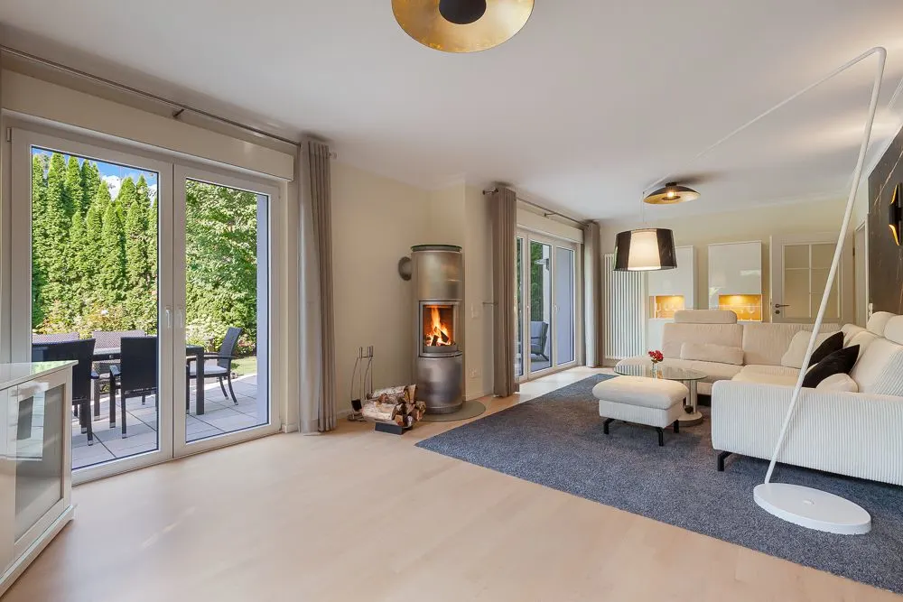 Modernes Wohnzimmer mit Kamin, Ecksofa, Teppich und Blick auf die Terrasse mit Gartenmöbeln.
