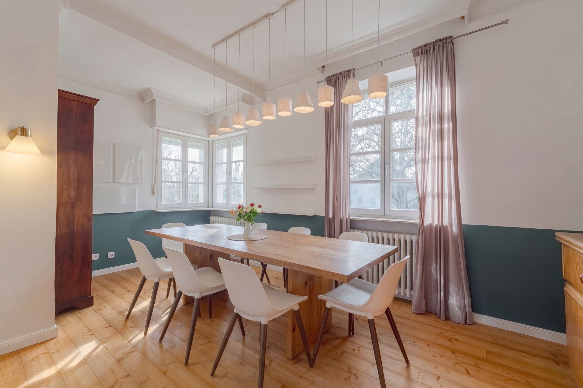 Heller Essbereich mit Holztisch, weißen Stühlen und großen Fenstern mit Vorhängen.