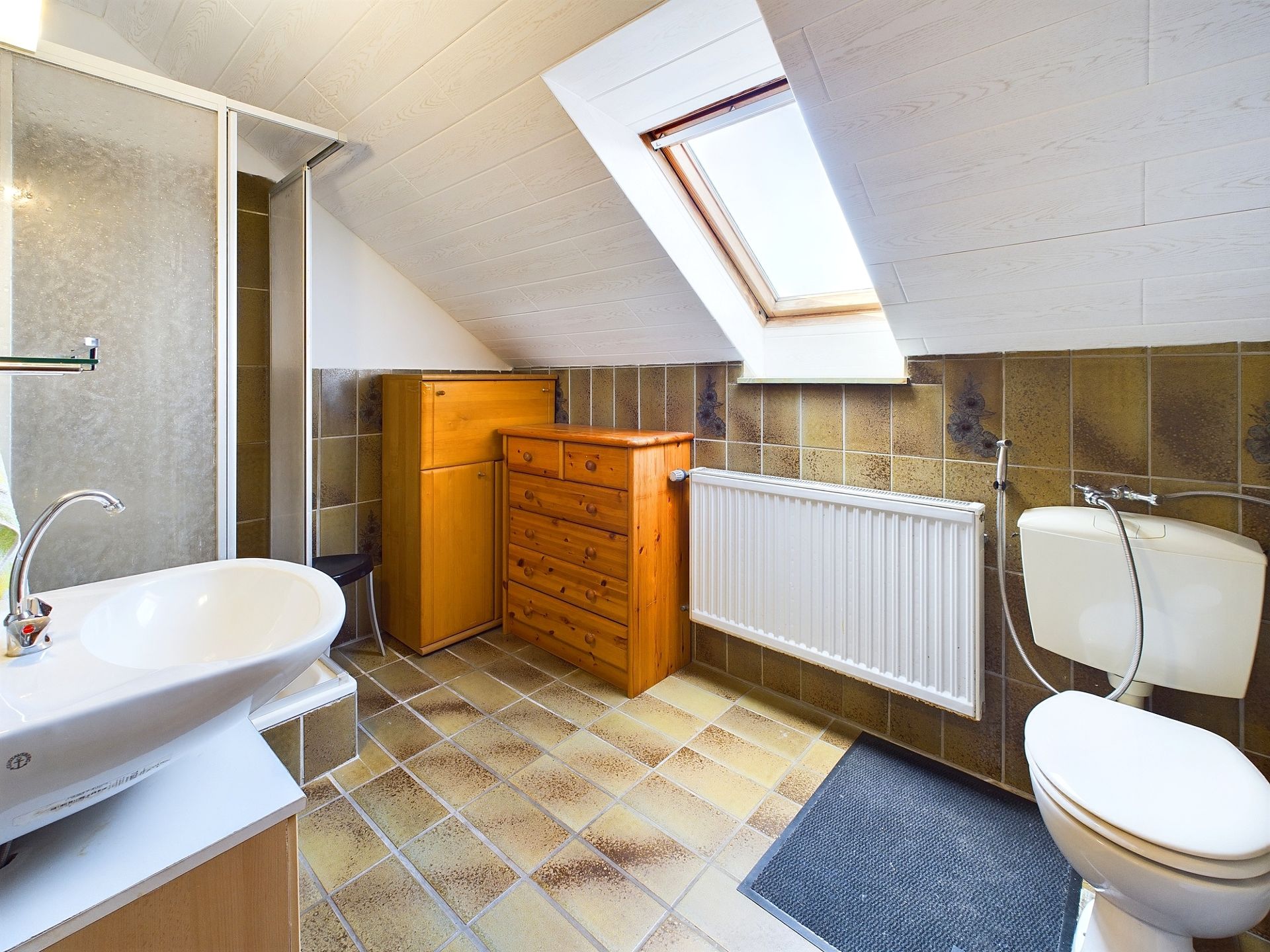 Badezimmer mit Waschbecken, Toilette, Dusche, Holzkommoden und Dachfenster.