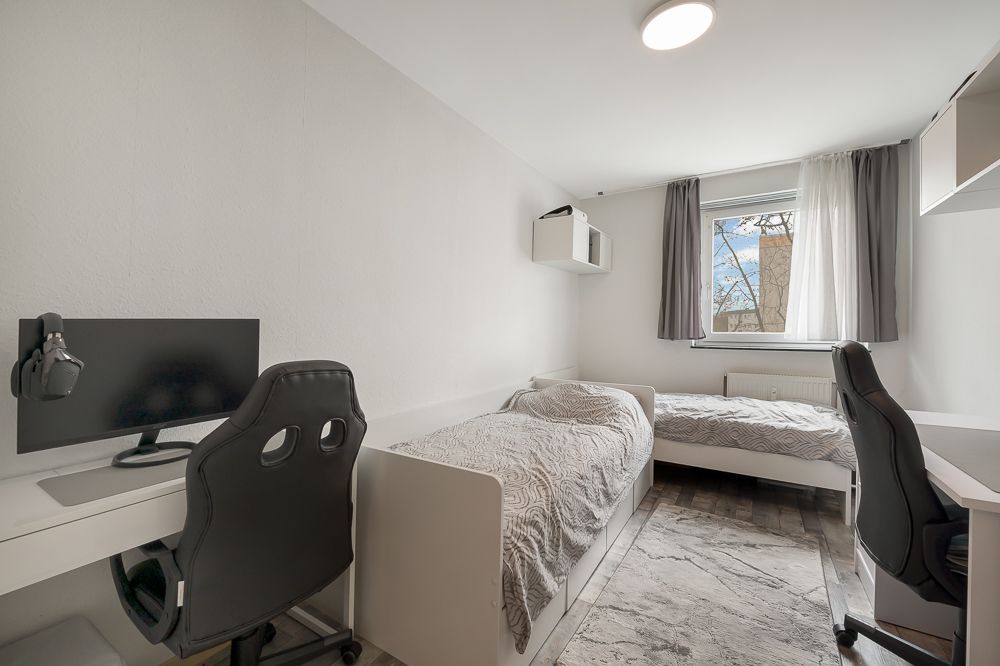 Helles Schlafzimmer mit zwei Einzelbetten, zwei Schreibtischen und einem Fenster mit Vorhängen.