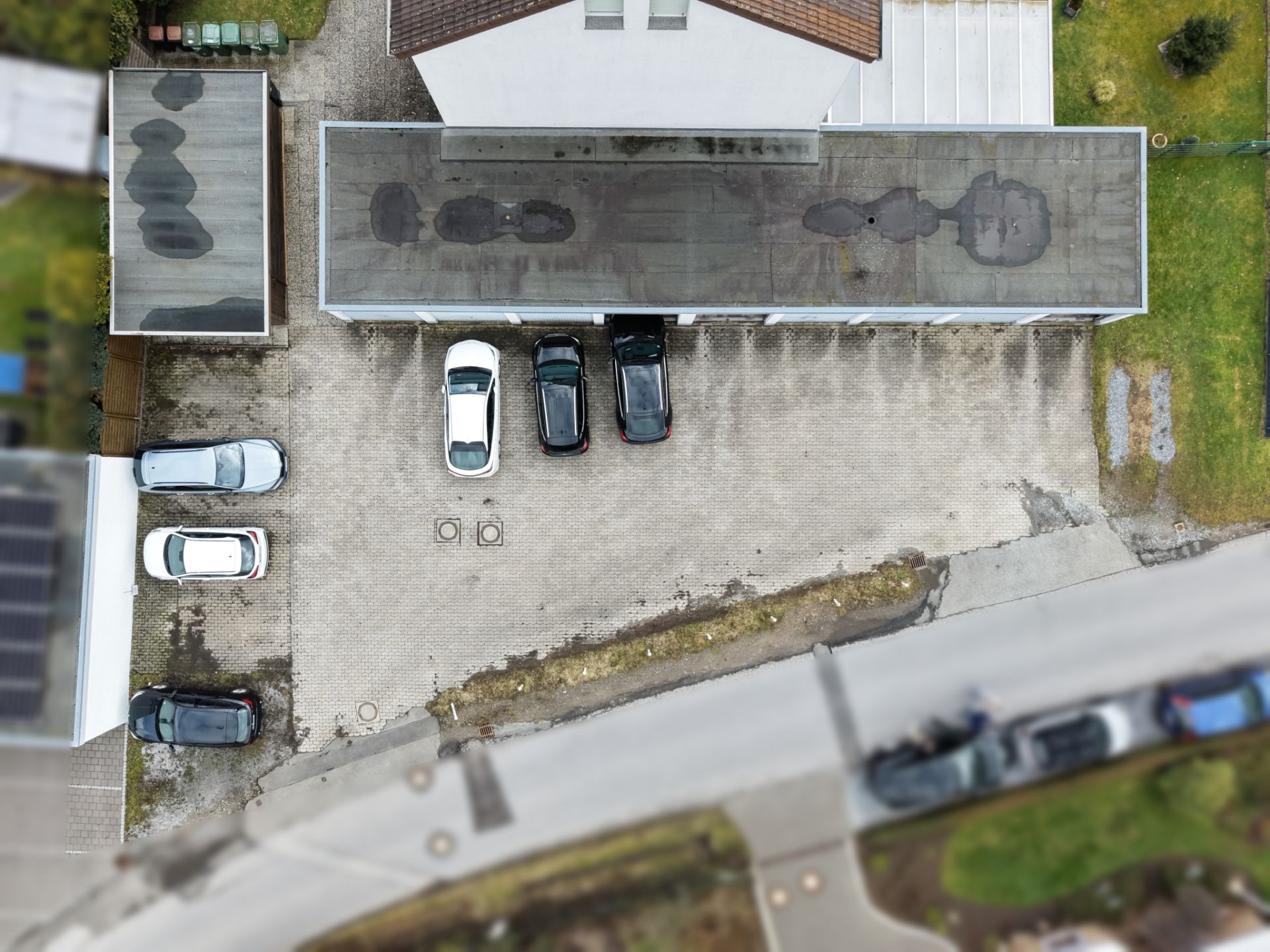 Luftaufnahme eines Parkplatzes mit mehreren geparkten Autos vor einem Wohngebäude.