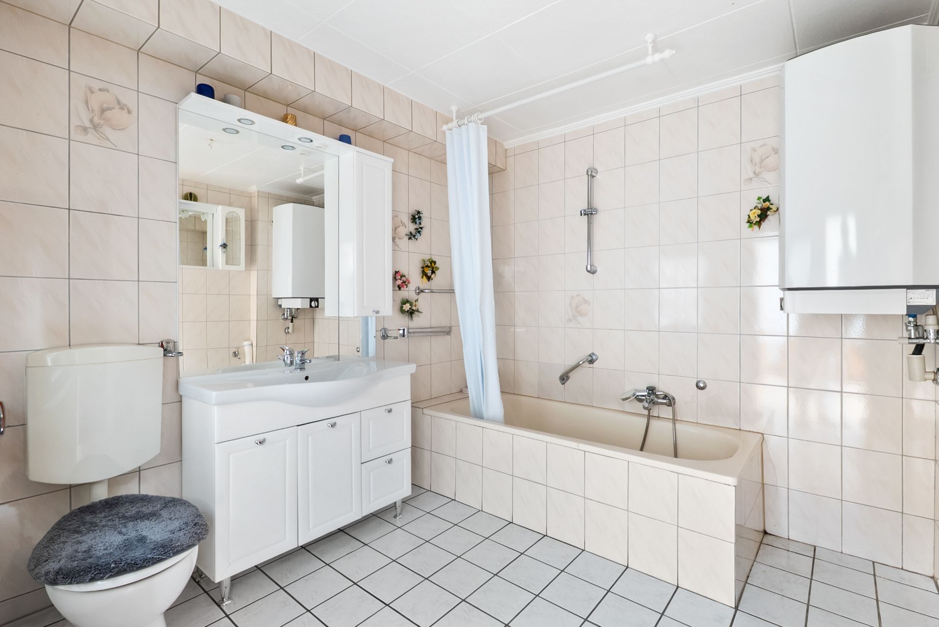 Helles Badezimmer mit Badewanne, Waschbecken, Spiegel, Toilette und weißen Fliesen.