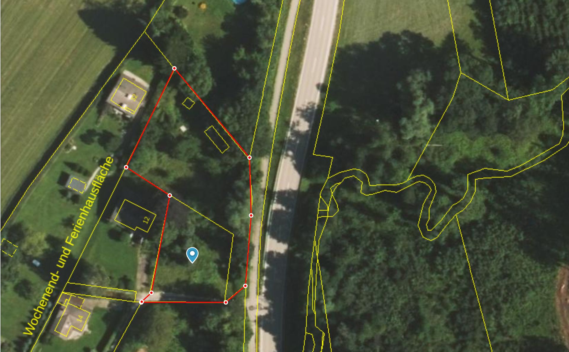 Luftbild einer Grundstücksfläche mit roten und gelben Umrisslinien neben einer Straße und Bäumen.