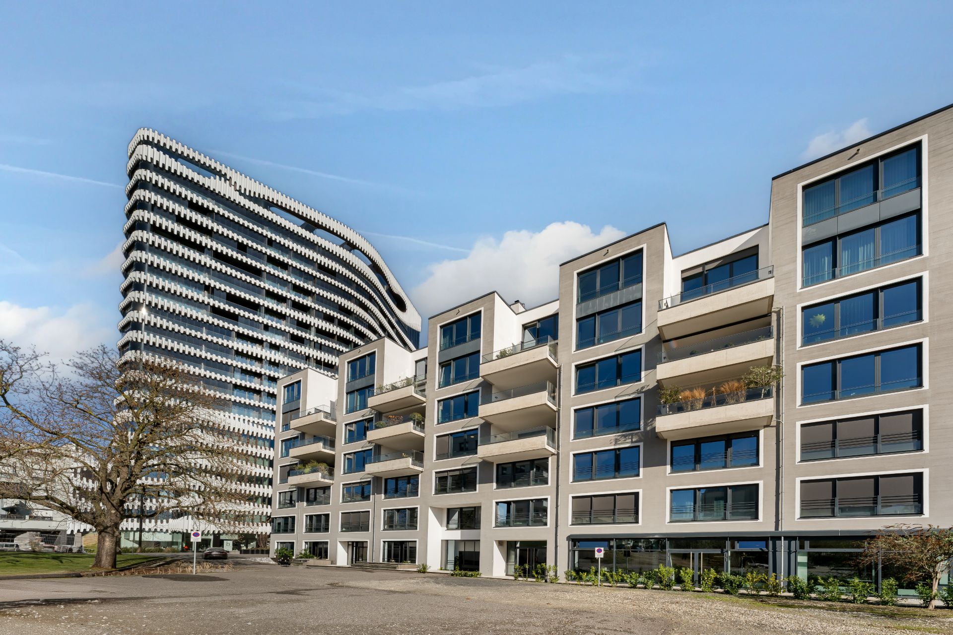 Moderne Wohngebäude mit vielen Balkonen und großen Fenstern, daneben ein markantes Hochhaus.