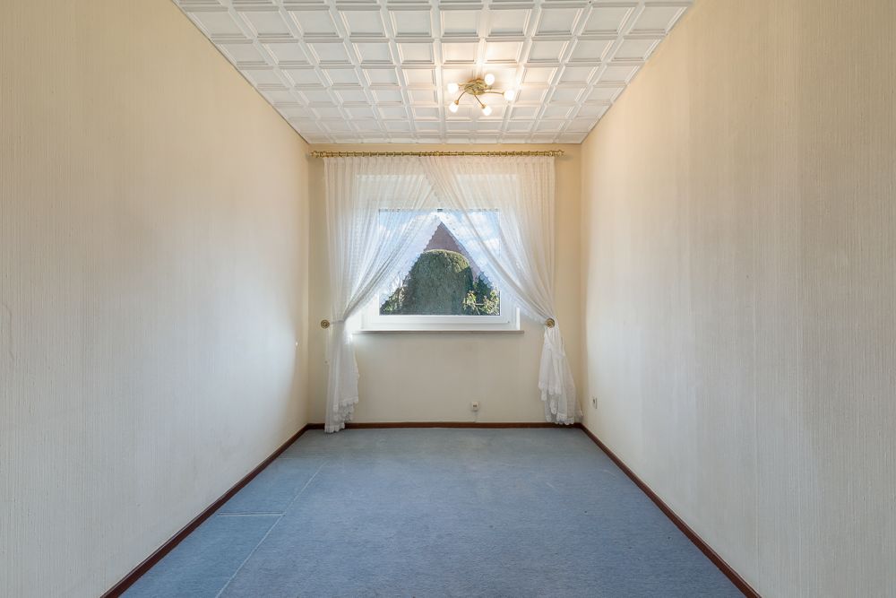 Leerer Raum mit Teppichboden, Fenster mit weißen Vorhängen und Deckenleuchte.