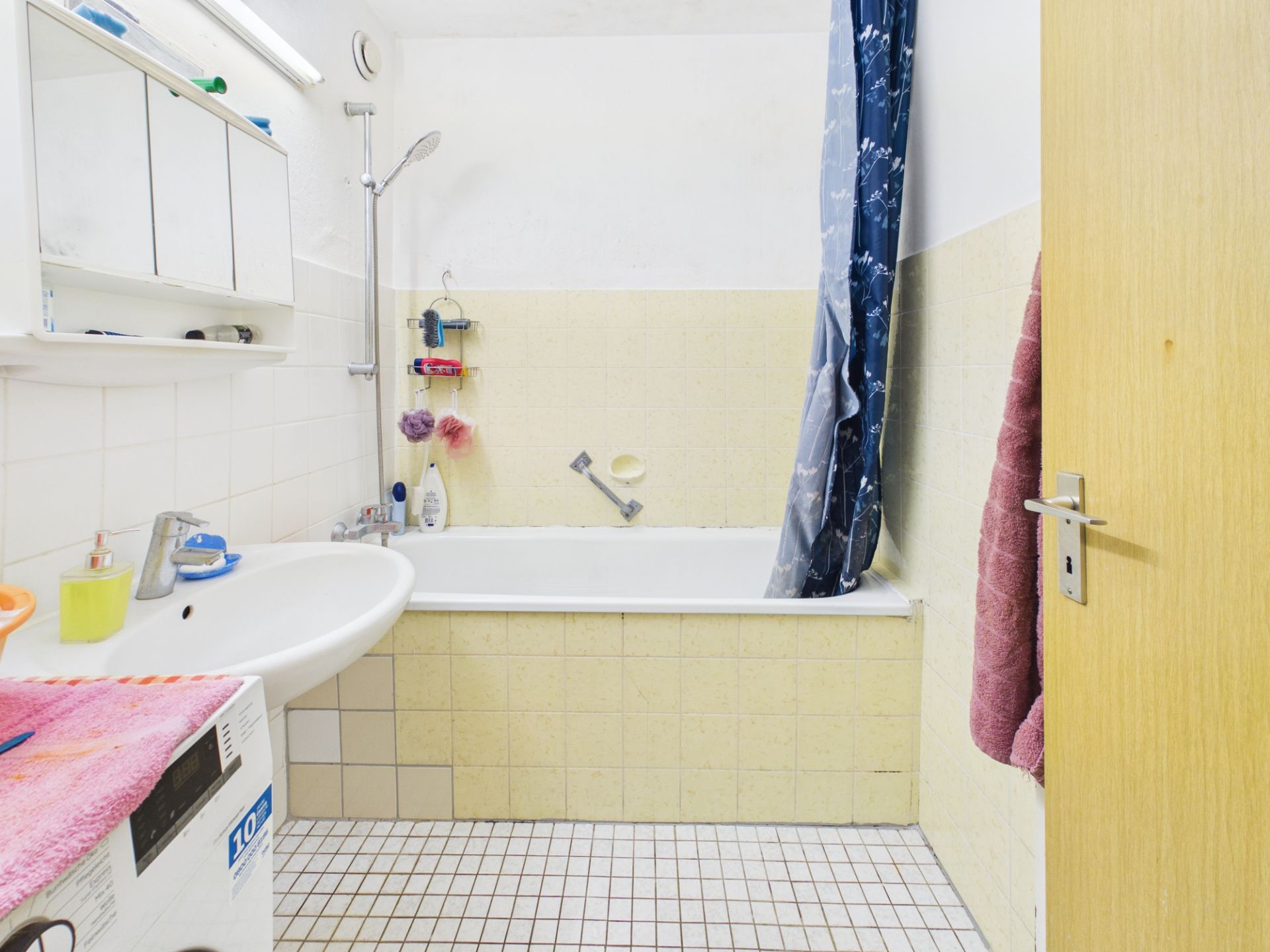 Badezimmer mit Badewanne, Waschbecken, Spiegel und Duschvorhang, hell gefliest.