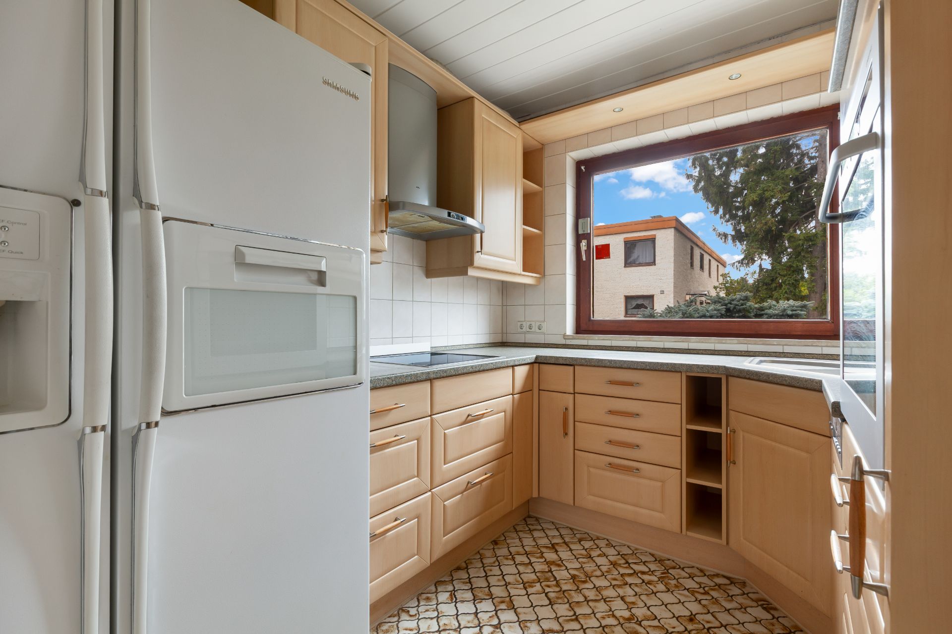 Helle Einbauküche mit großem Fenster, Kühlschrank und Holzschränken.