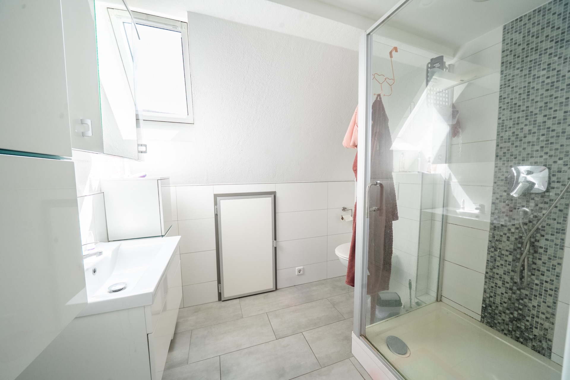 Helles Badezimmer mit Dusche, Waschbecken, Fenster und Wandfliesen.