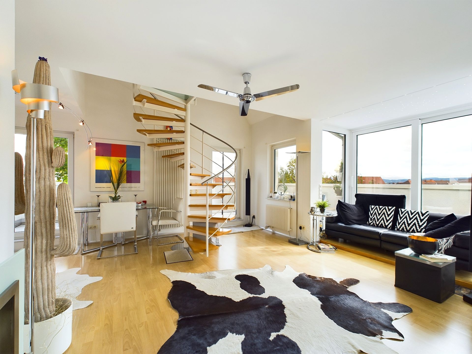 Helles Wohnzimmer mit Wendeltreppe, schwarzem Sofa und großem Fenster, Holzboden und Teppich.