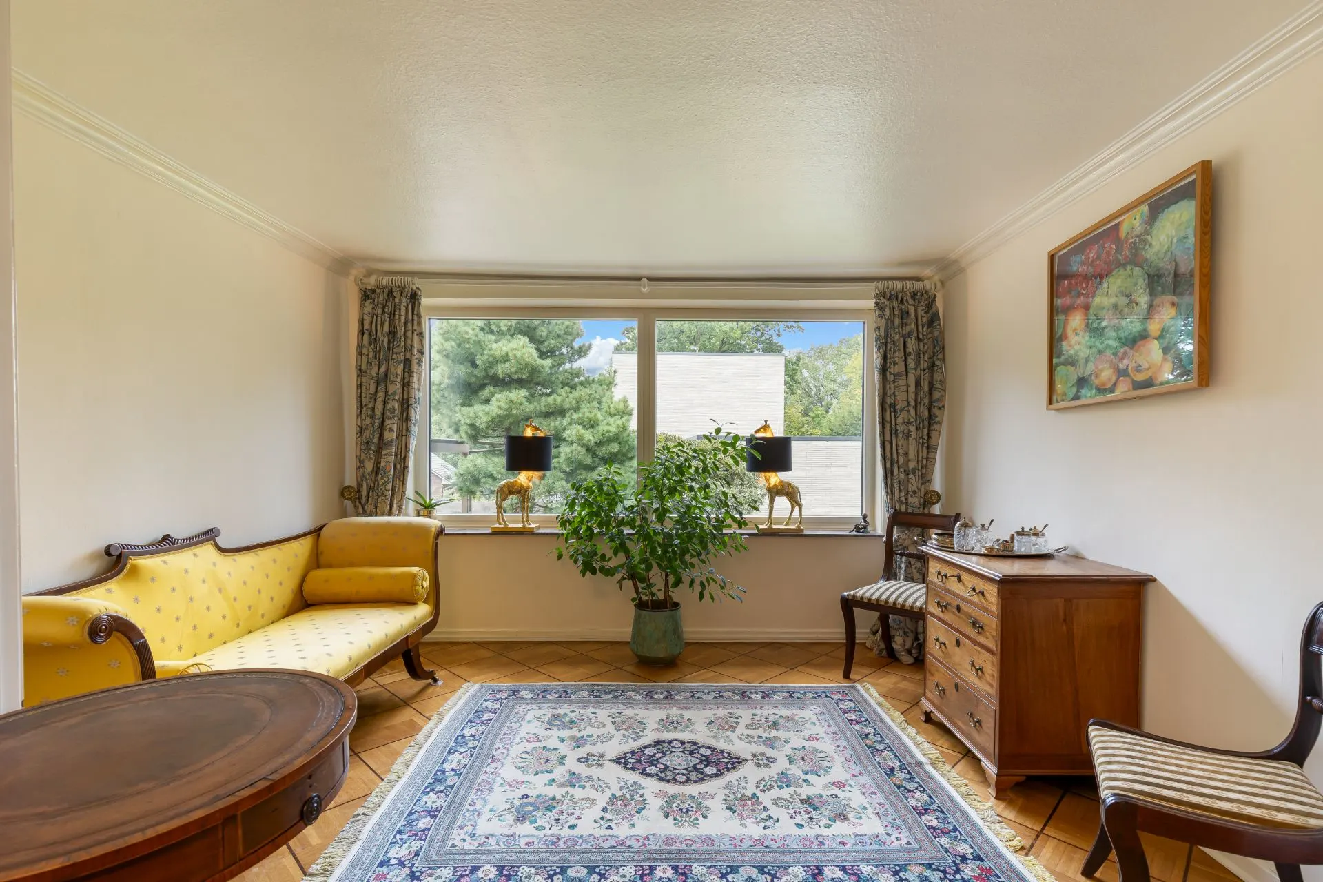 Helles Wohnzimmer mit gelbem Sofa, Teppich, Holzmöbeln und großem Fenster mit Blick ins Grüne.